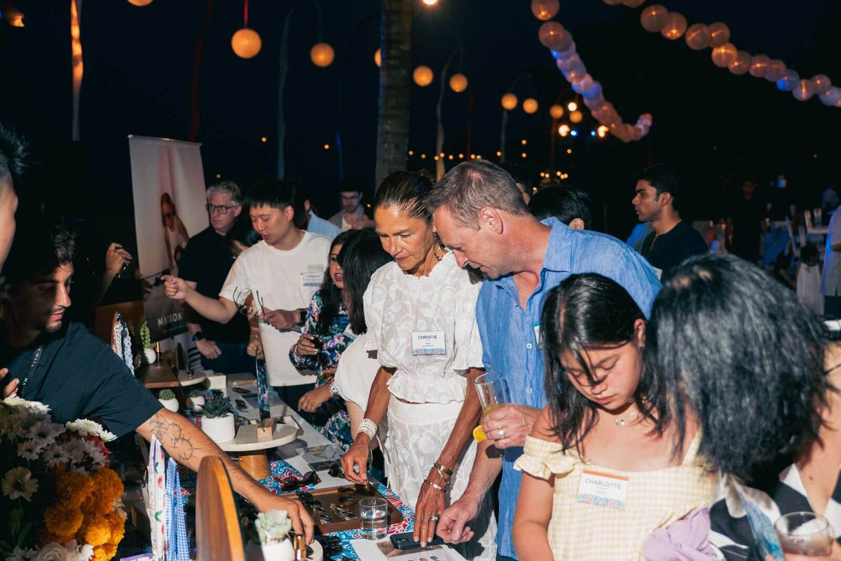 Guests trying on Maison Mata sunglasses at an evening event by the beach in Bali
