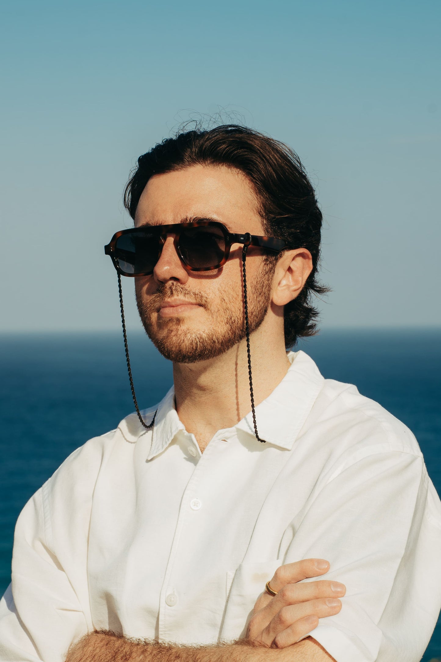 Man in Luxe Co. Caramel Swirl tortoise sunglasses and eyewear chain on the Bali coastline, Maison Mata