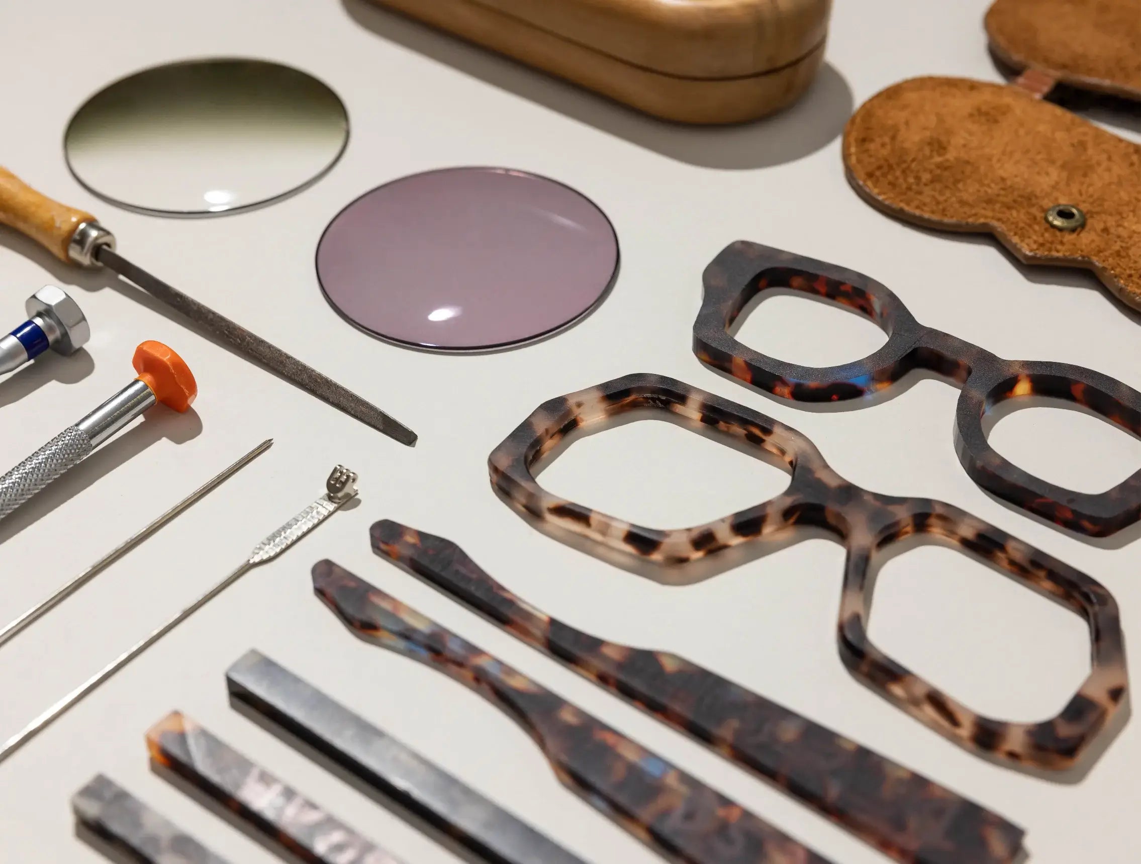Handmade eyewear components laid out for fabrication, including acetate, hinges, lenses and metal core for assembly.