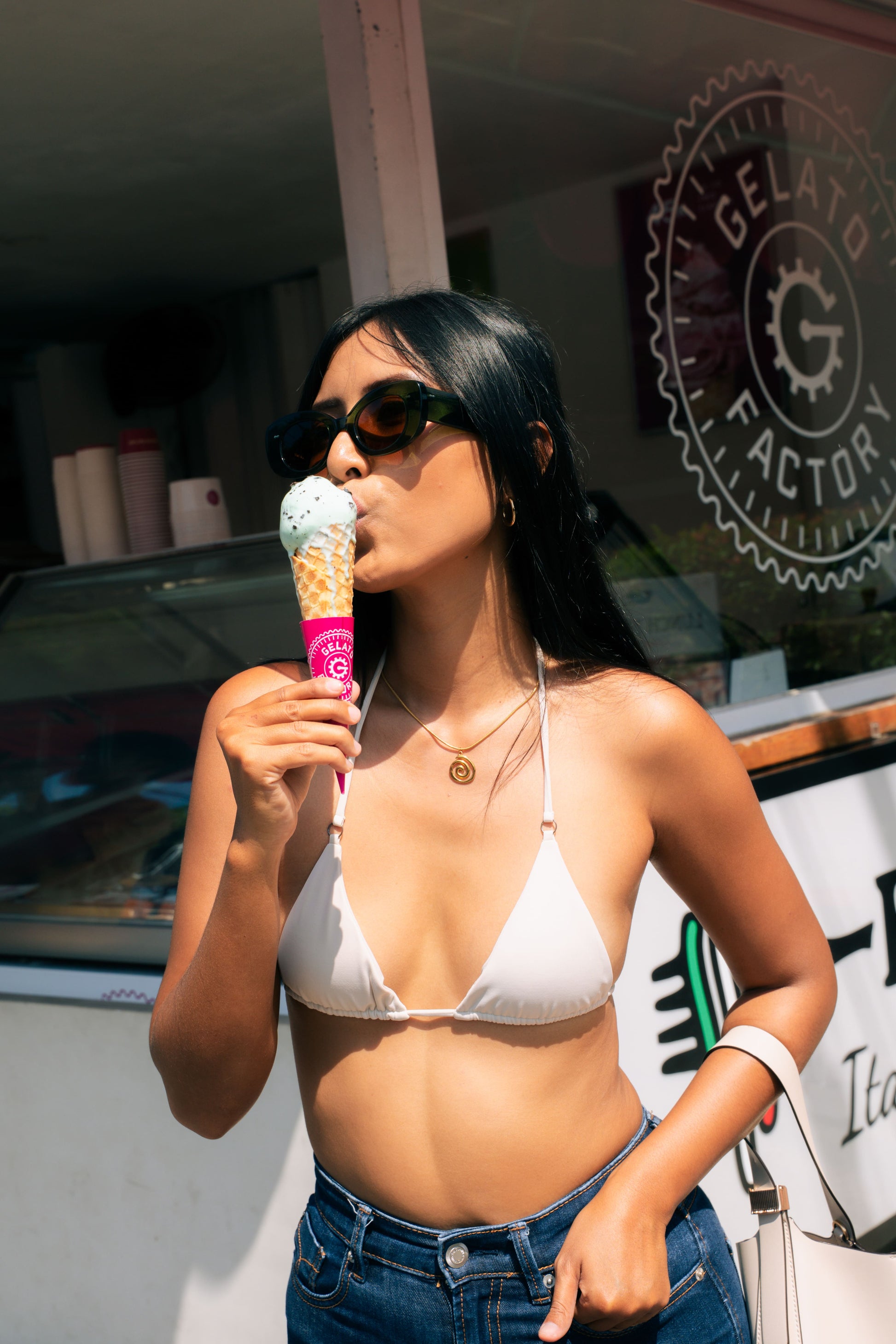 امرأة ترتدي نظارة Maison Mata الشمسية بترفلاي بلون Bali Blue Olive Gove، تتناول الجيلاتو تحت شمس بالي.