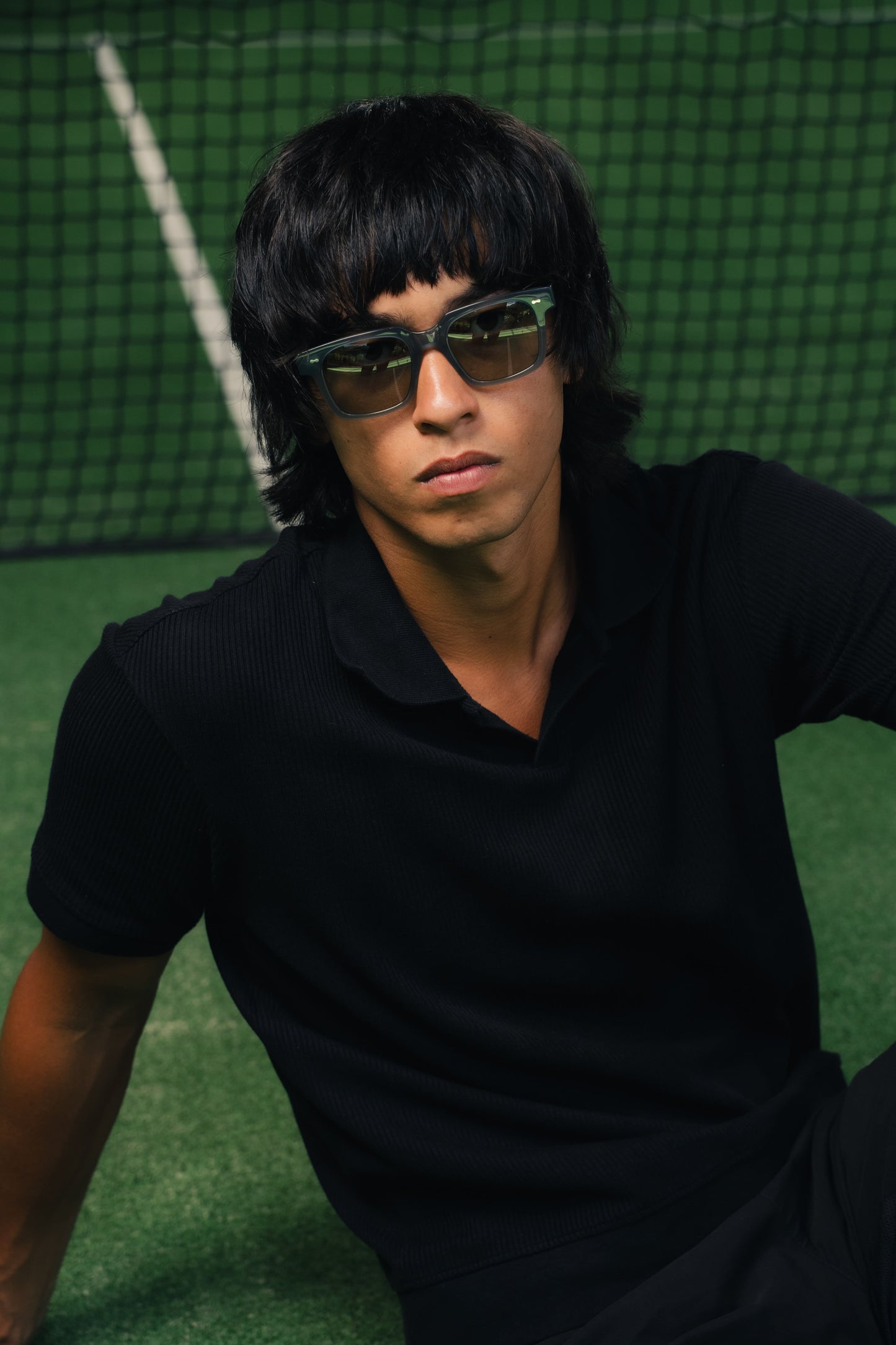 Man in Borneo Bliss Charcoal Cloud rectangular sunglasses on a green tennis court in Bali