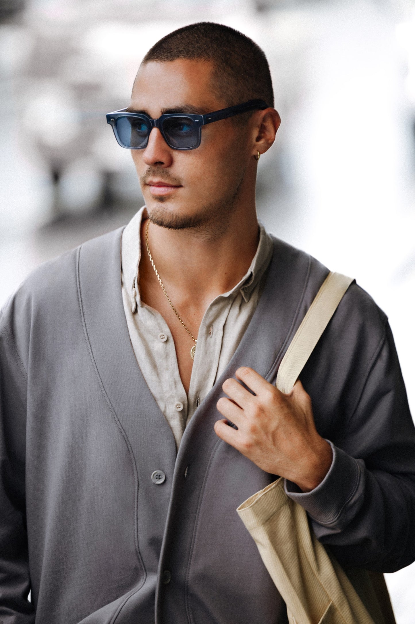 Man in Borneo Bliss Charcoal Cloud rectangular sunglasses and tote bag on a city street