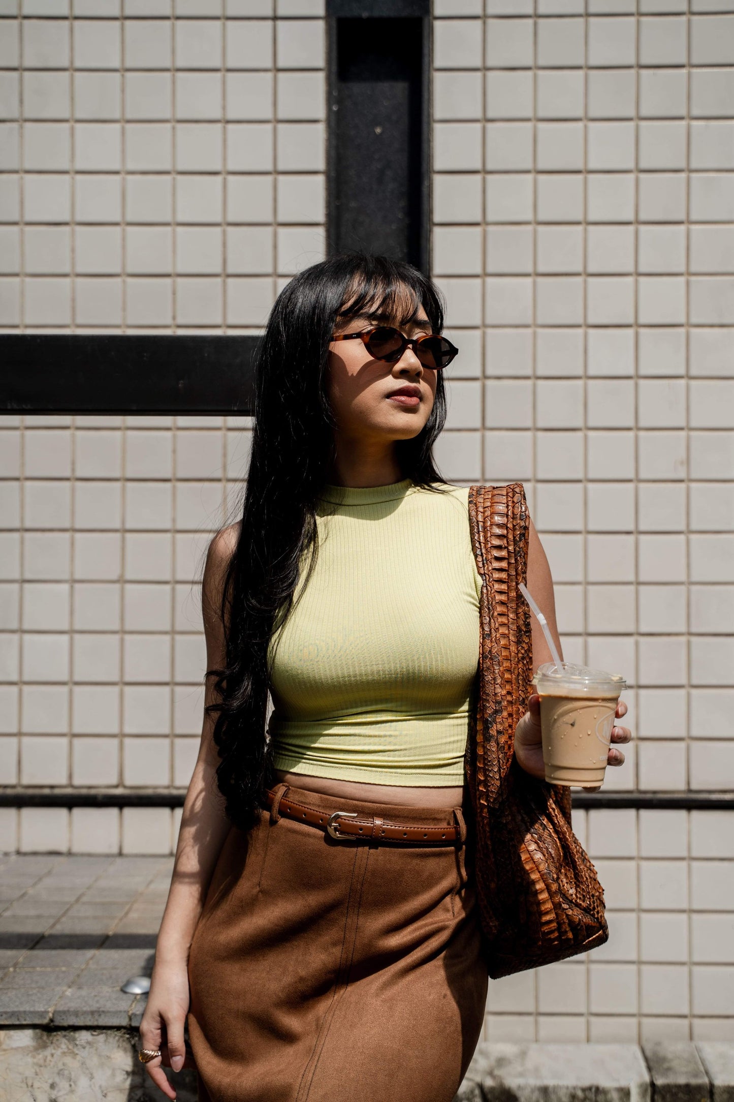 Woman in Cove Caramel Swirl oval sunglasses walking a Bali street in a brown skirt