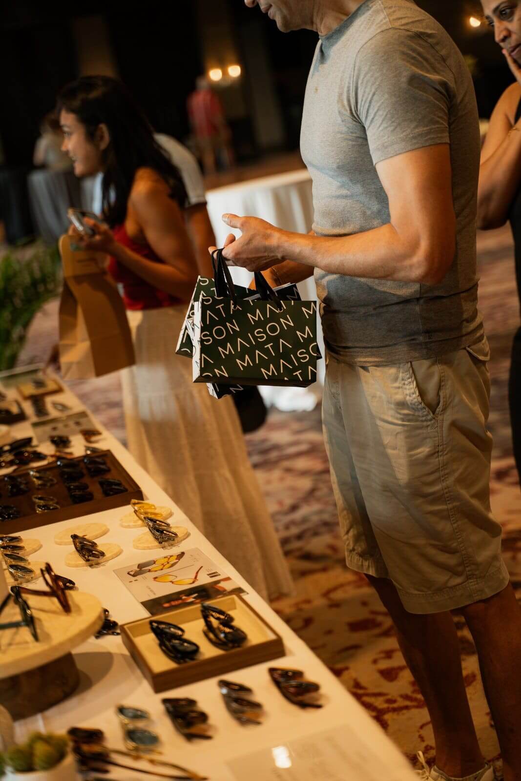 Guest holding a Maison Mata gift bag next to the sunglasses display at a corporate event