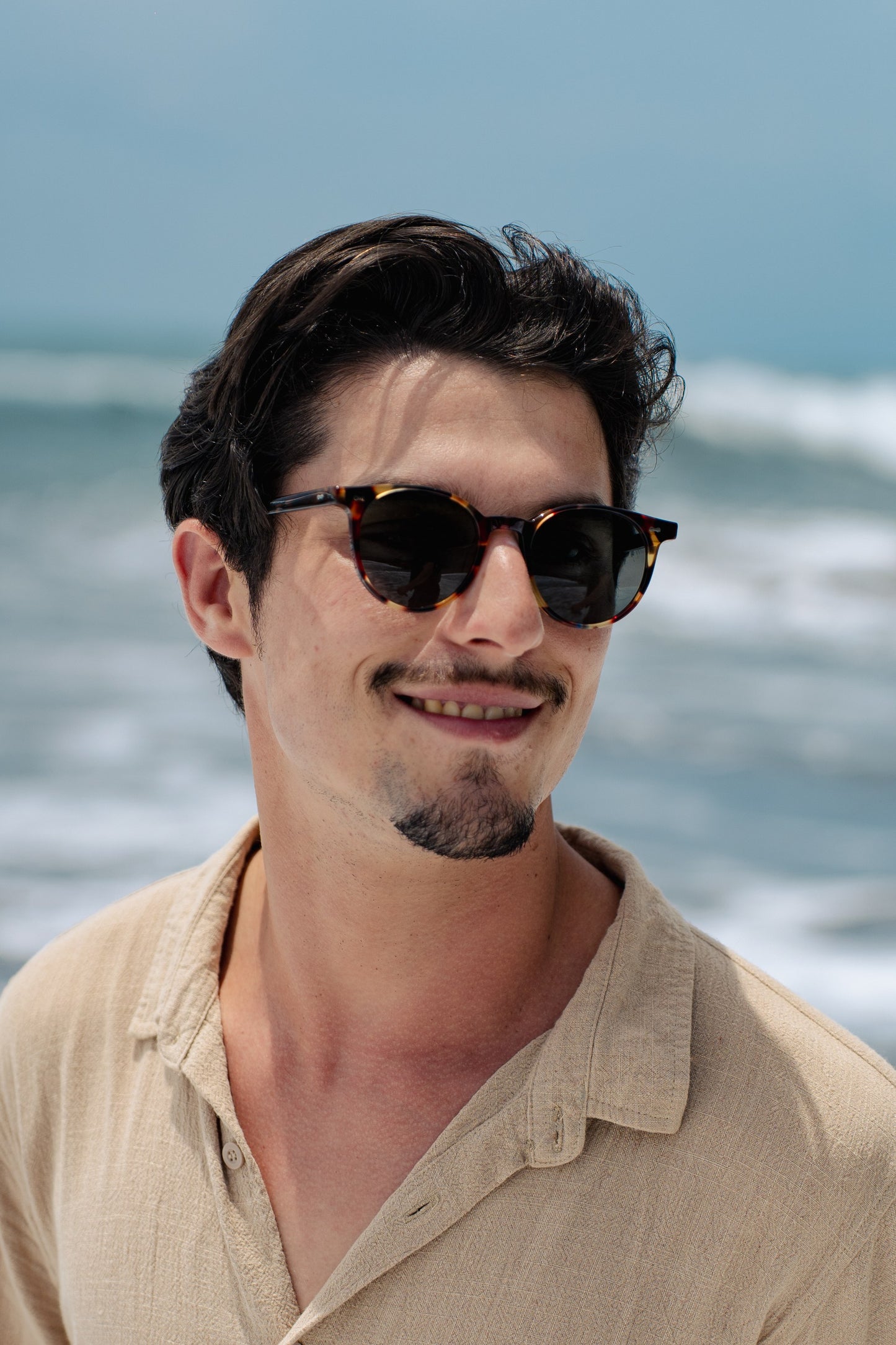 Portrait of man in Flores Breeze Morning Lagoon round sunglasses by the ocean