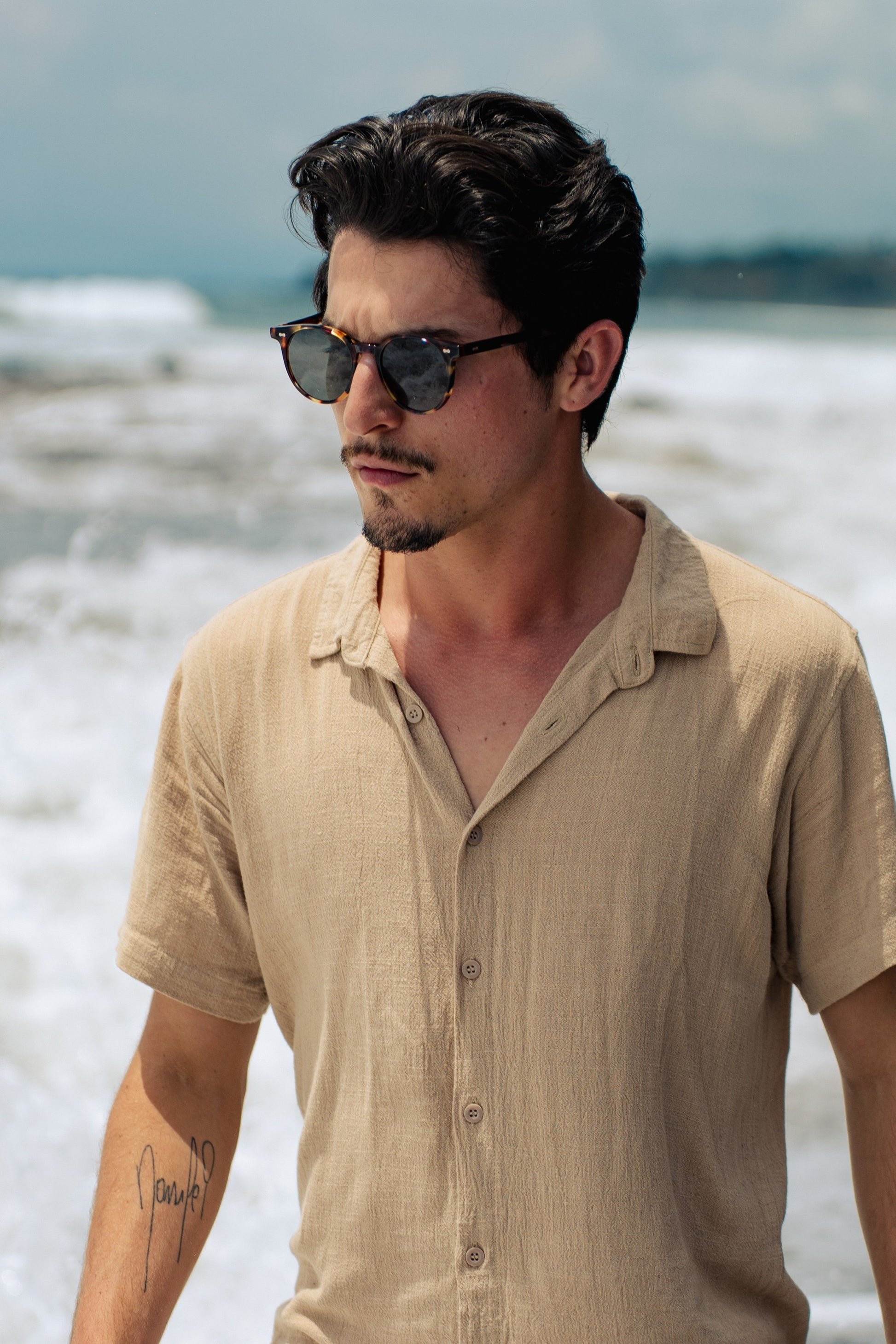 Man in Flores Breeze Morning Lagoon round acetate sunglasses on a Bali beach