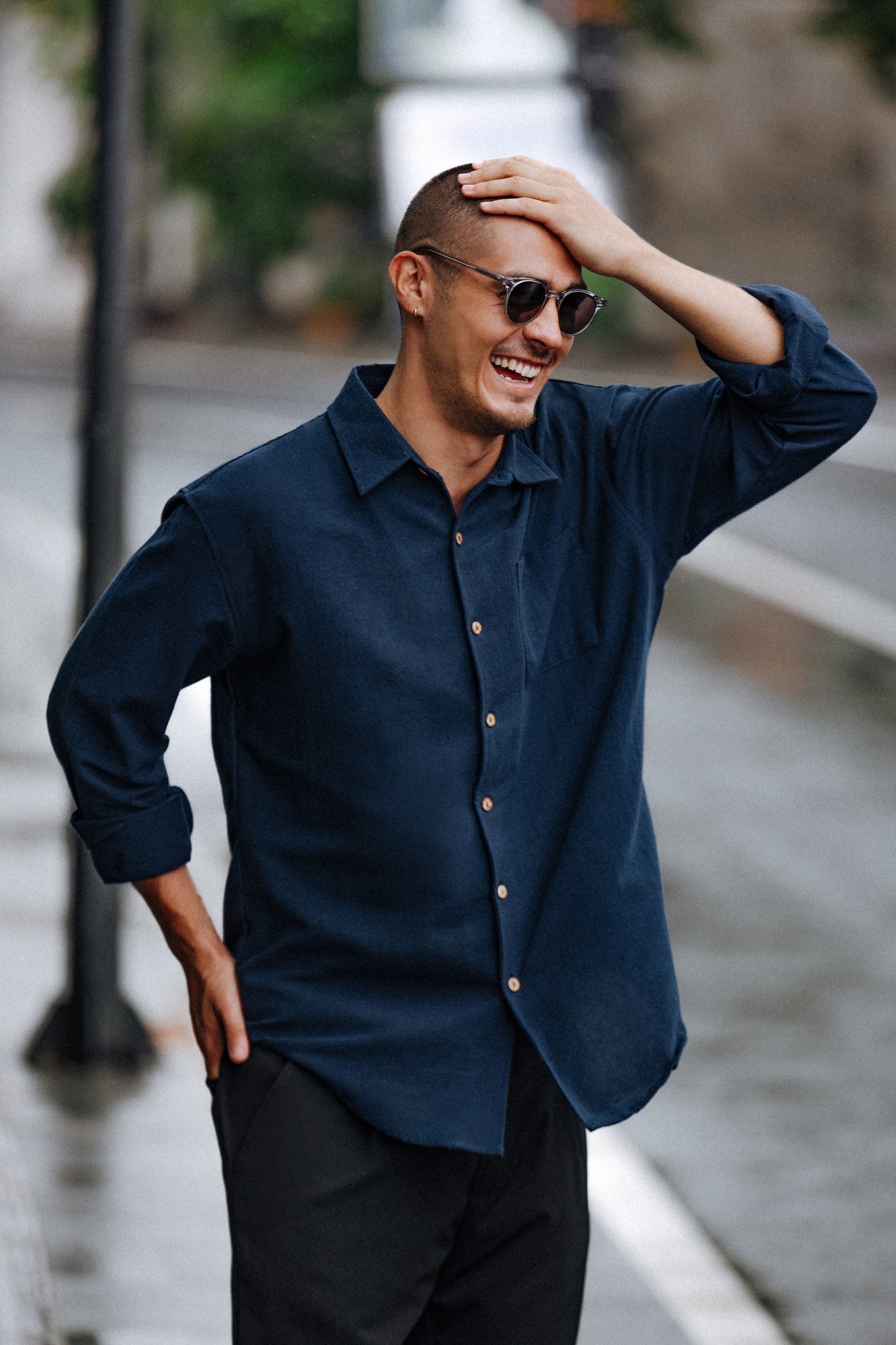 Man in Flores Breeze Silver Mist round sunglasses and navy linen shirt on a rainy street