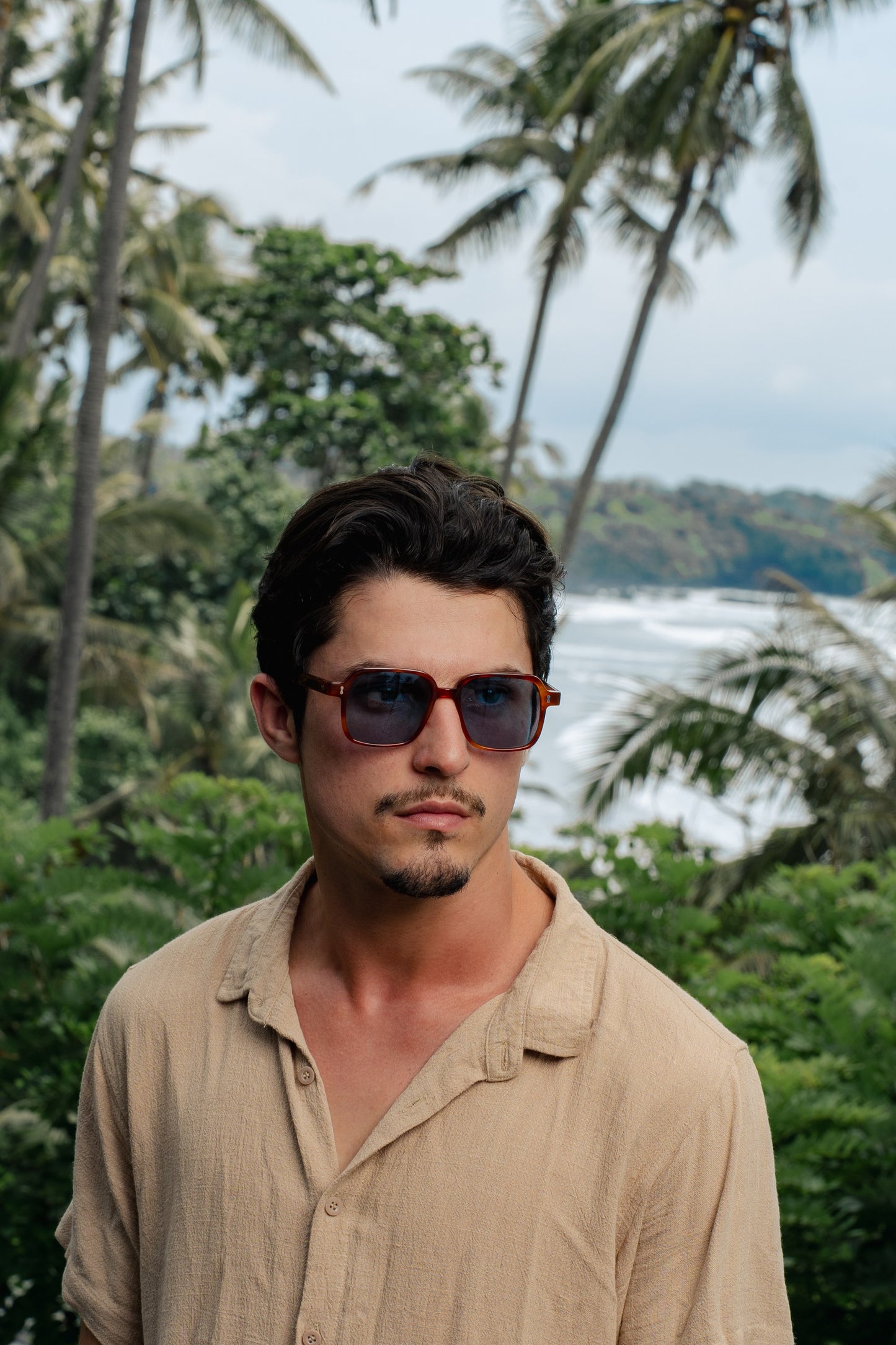 Man in Gili Escape Olive Gove square sunglasses in a tropical Bali garden