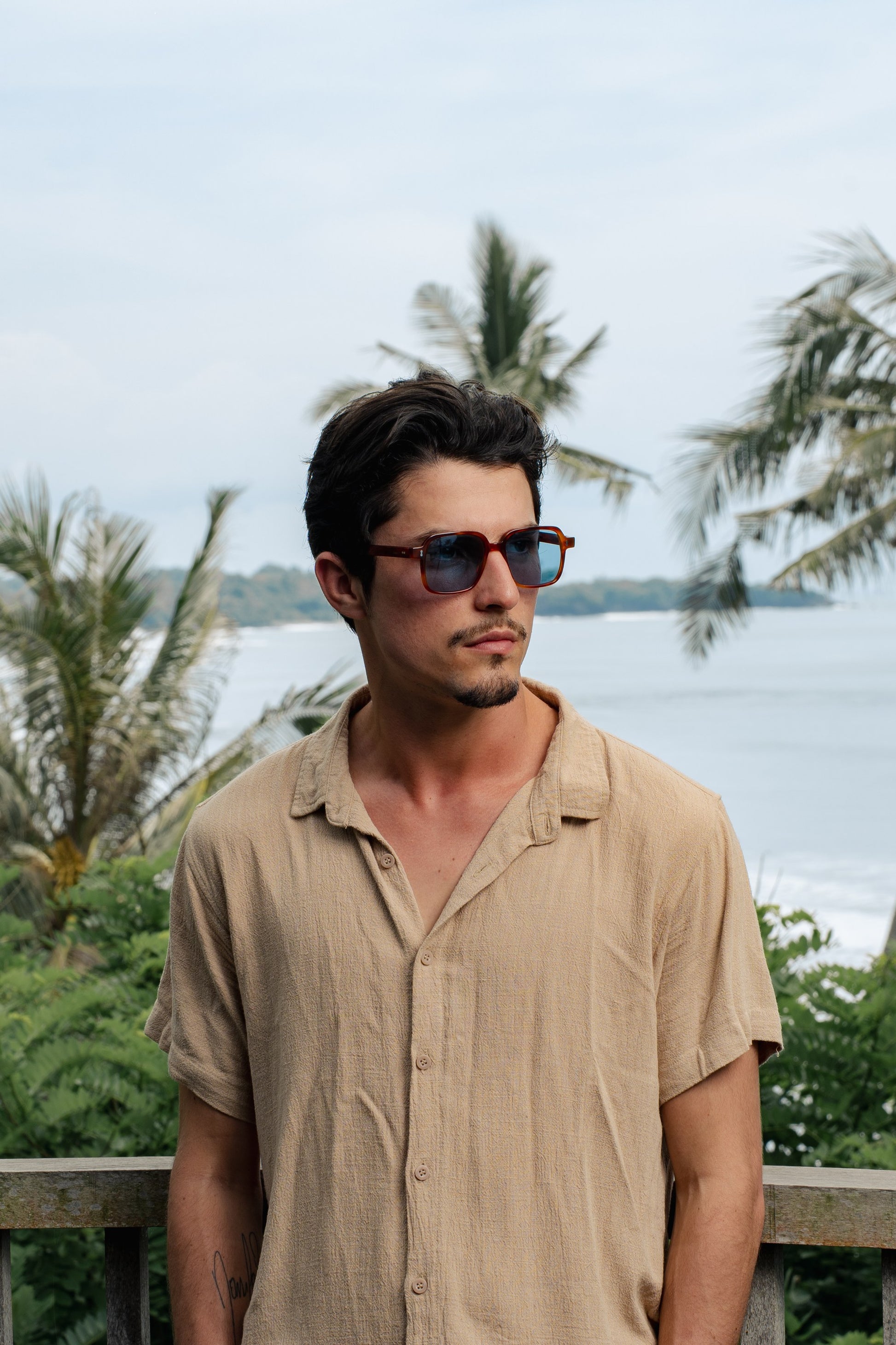 Man wearing Gili Escape Amber Sun bold square sunglasses by the Bali coast