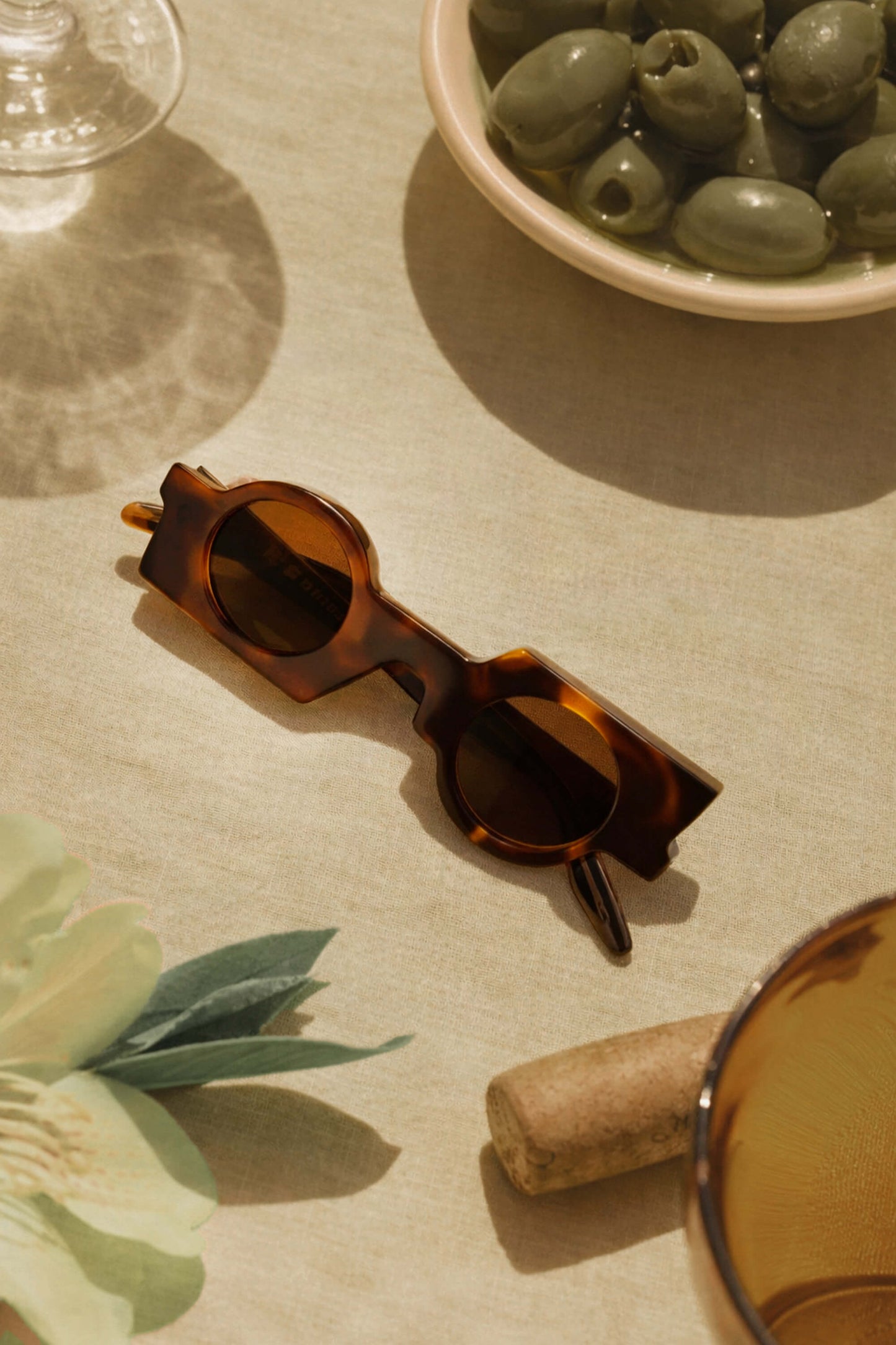 Maison Mata handmade tortoiseshell acetate geometric sunglasses on a linen table with olives and wine — lunettes de soleil géométriques acétate écaille sur table en lin — kacamata geometris asetat tortoise di meja linen — gafas geométricas carey sobre mesa de lino — Bali handmade eyewear