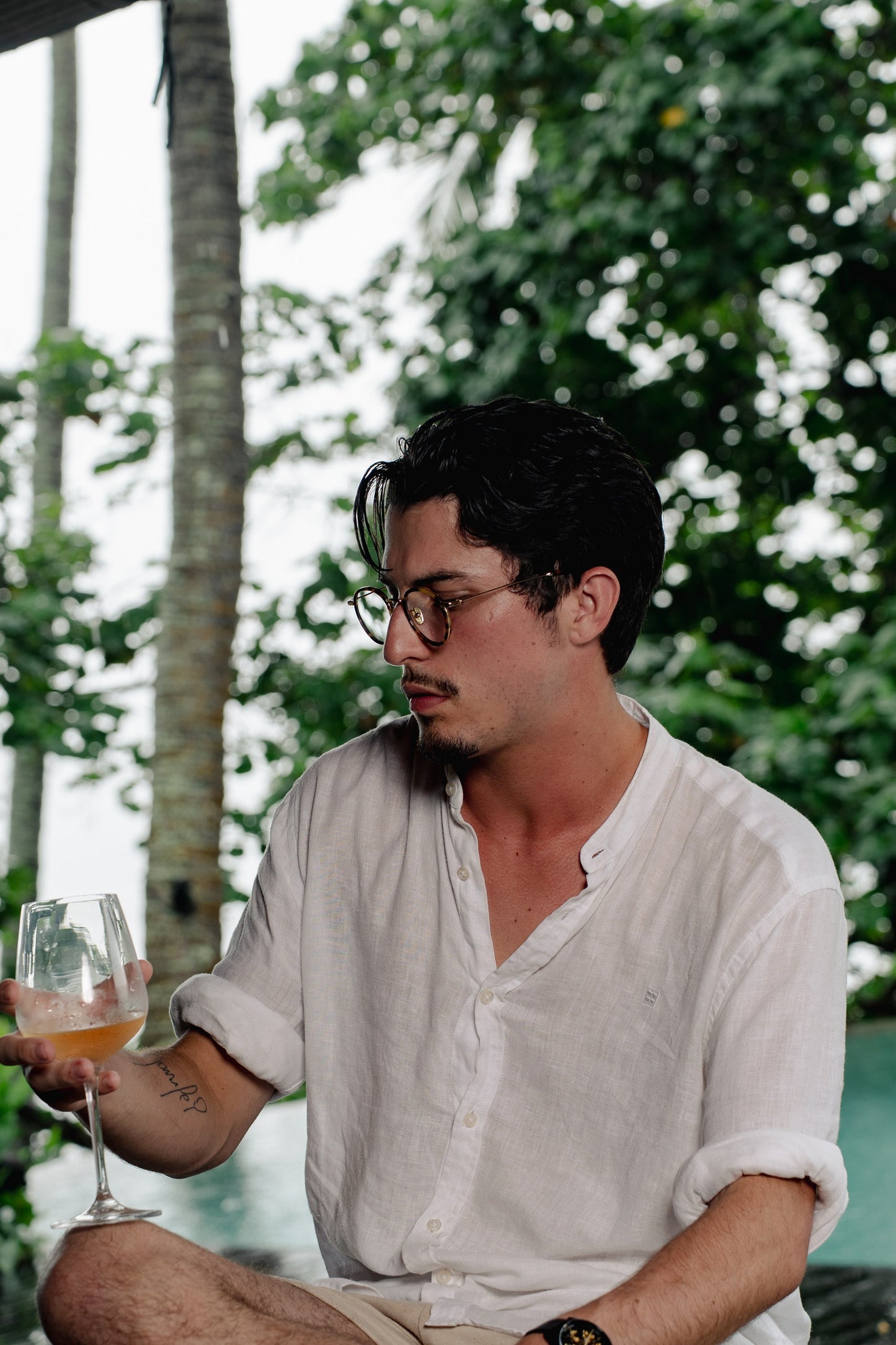 Man in Java Jungle Sunset Glow round eyeglasses holding a glass of wine in Bali