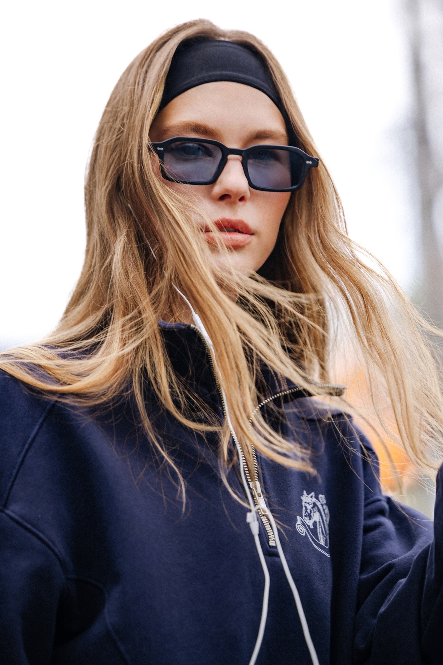 Woman in Komodo Rise Velvet Noir rectangular sunglasses and navy sweatshirt outdoors