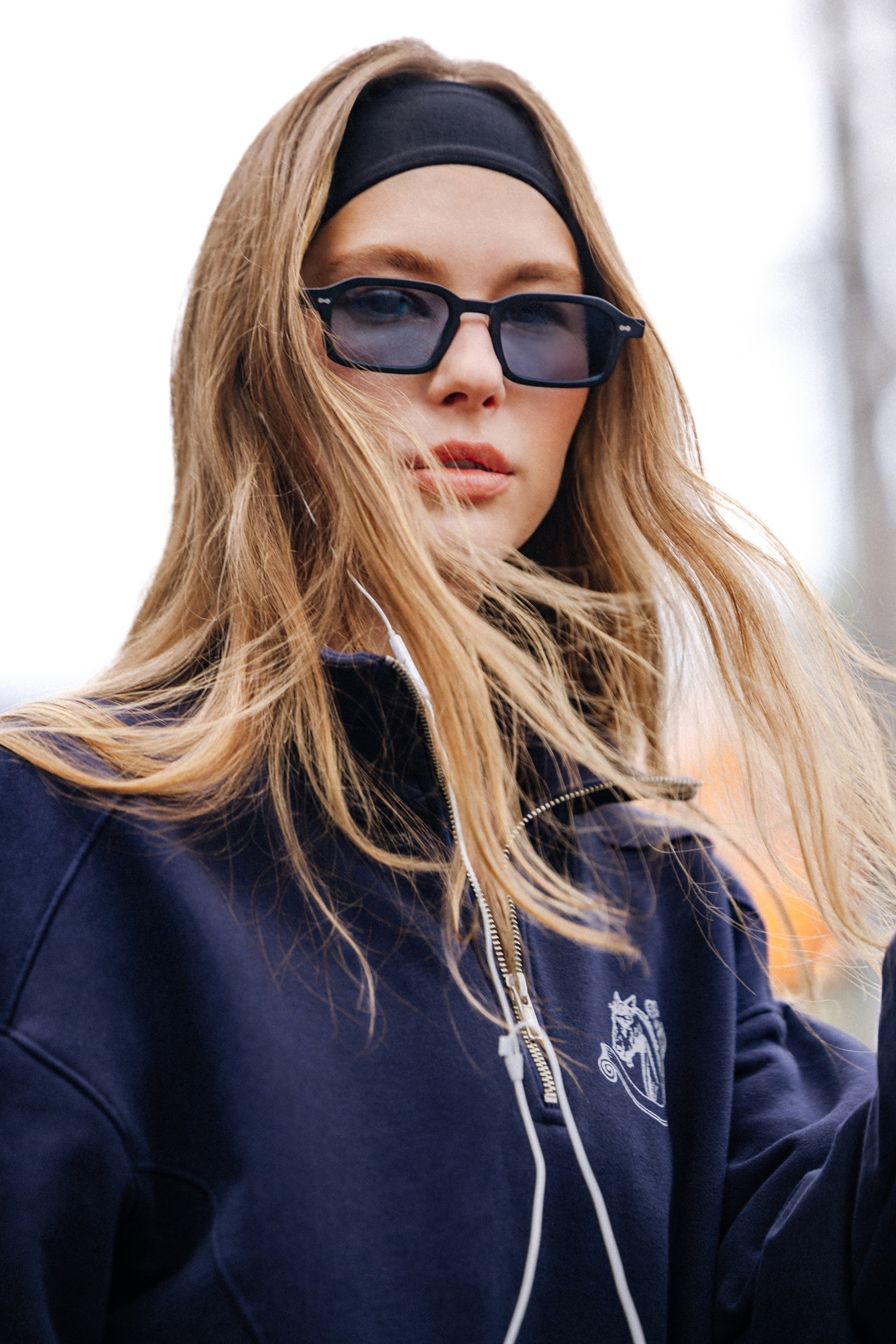 Woman in Komodo Rise Velvet Noir rectangular sunglasses and navy sweatshirt outdoors
