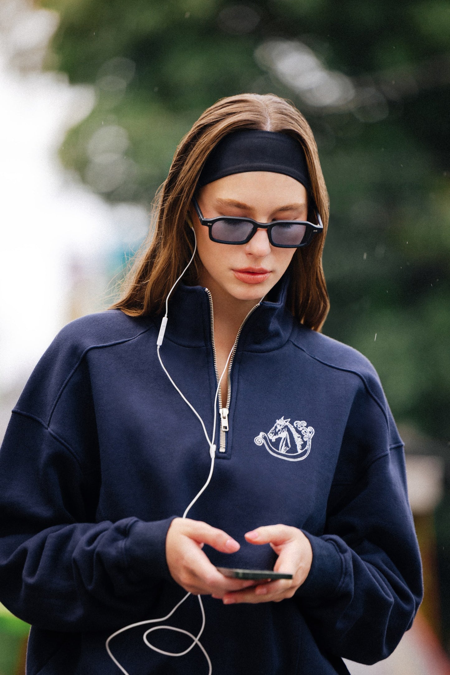 Woman wearing Komodo Rise Velvet Noir slim rectangular sunglasses on a rainy day