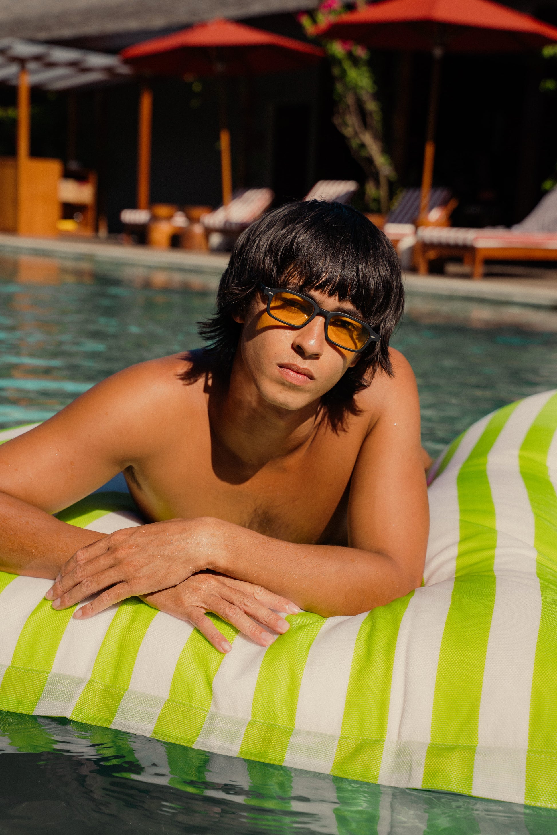 Man in Komodo Rise Velvet Noir sunglasses with yellow tinted lenses on a pool float in Bali
