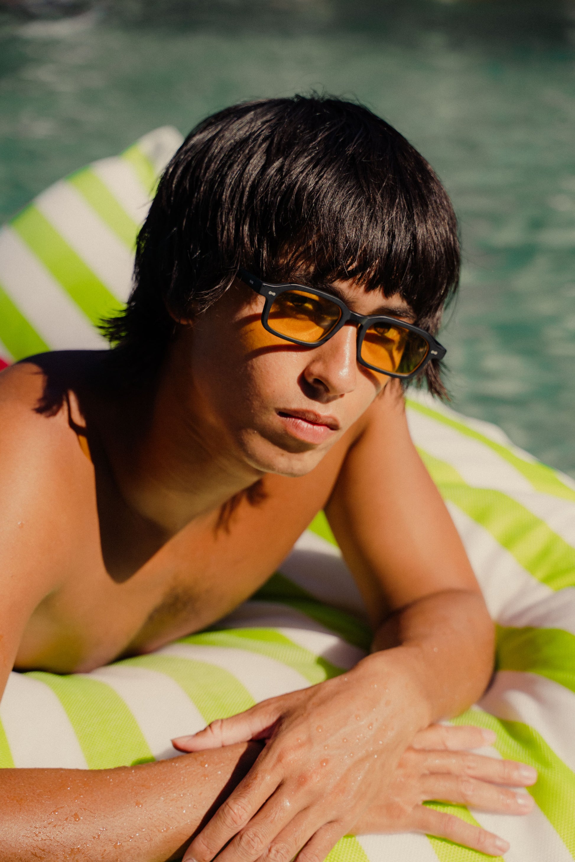 Man wearing Komodo Rise Velvet Noir black acetate sunglasses with workshop yellow tint Bali pool