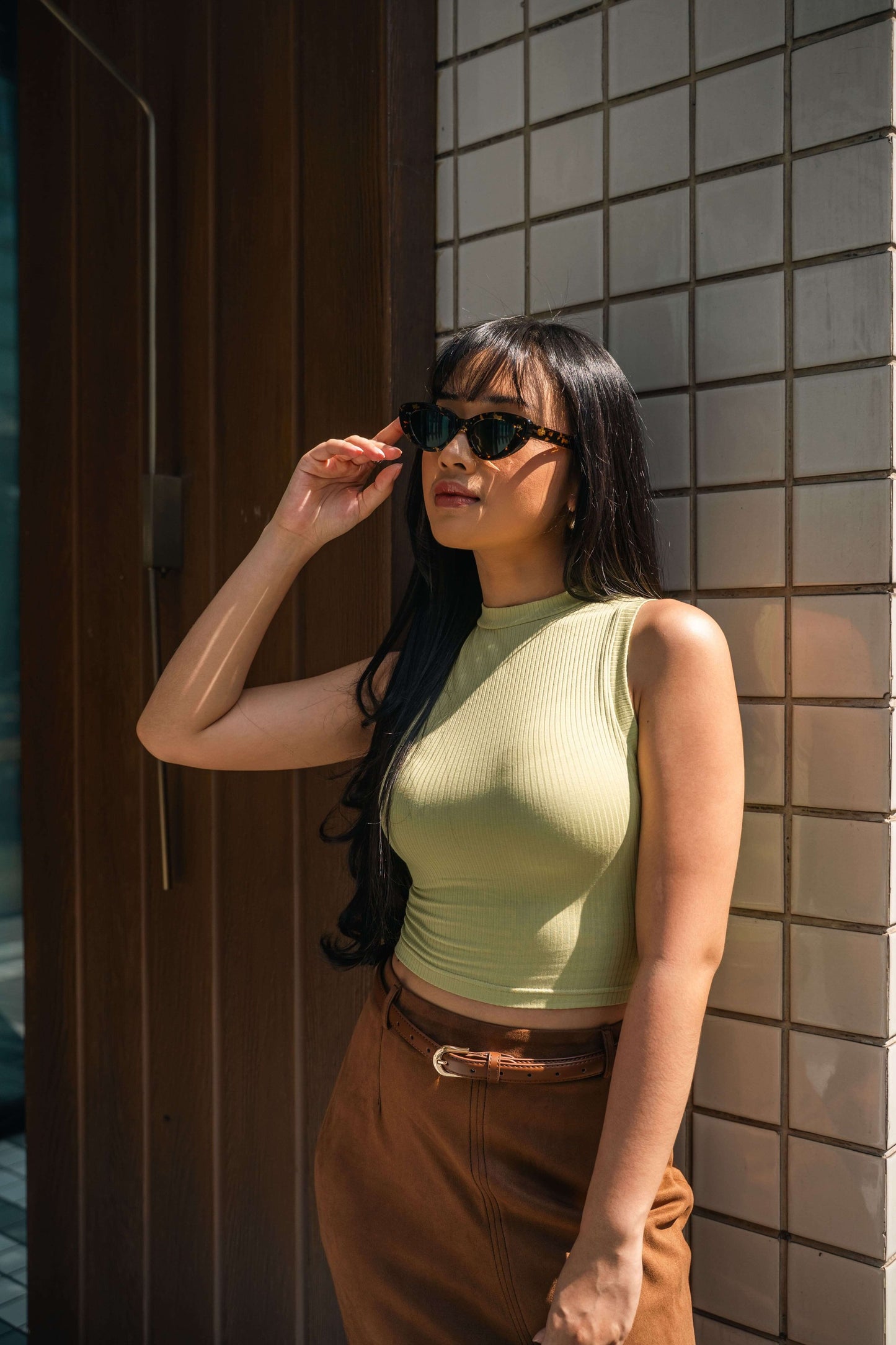 Woman in Lombok Luxe Black Sun cat-eye sunglasses against a tiled wall in Bali