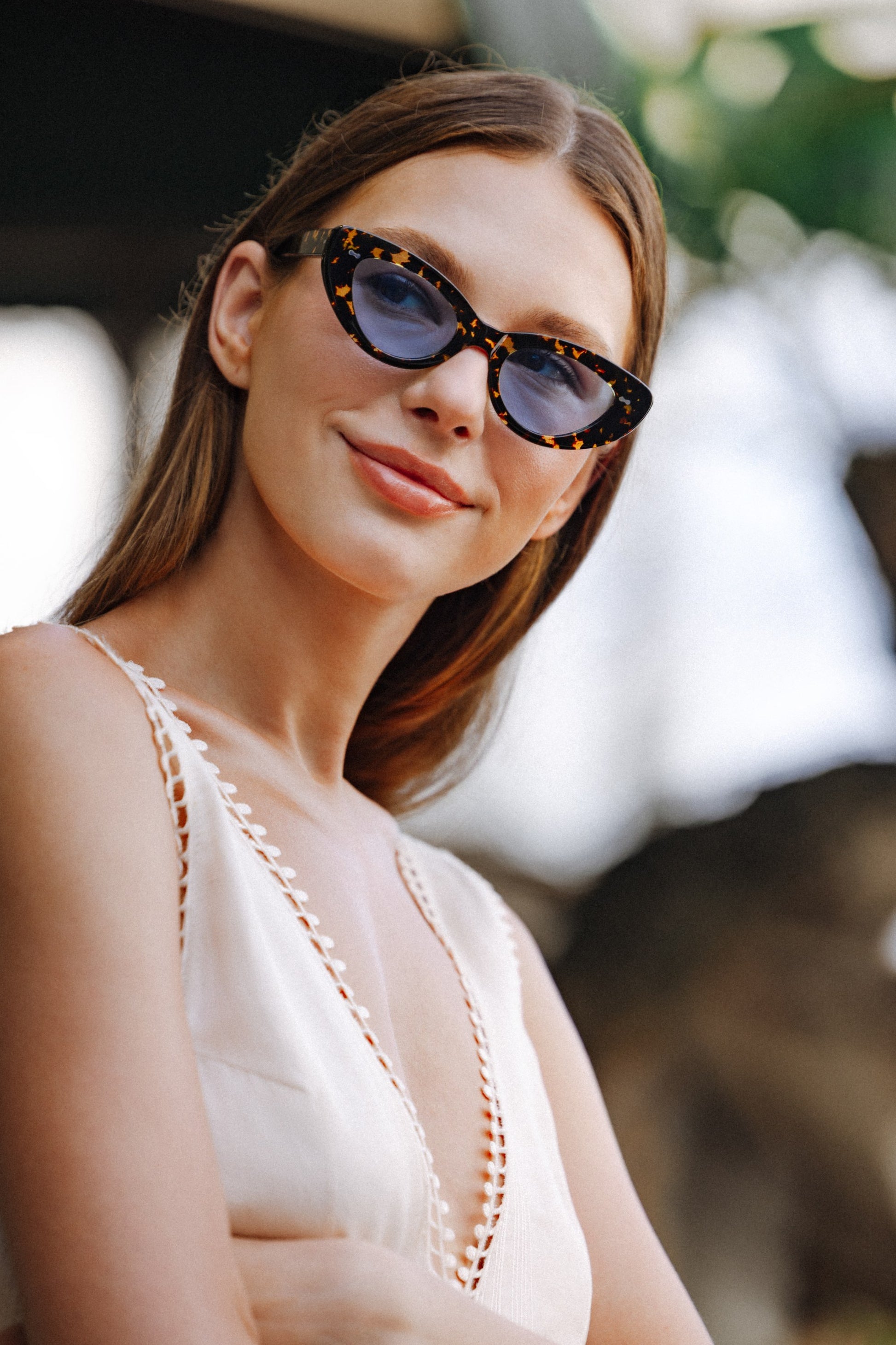 Smiling woman in Lombok Luxe Black Sun cat-eye sunglasses and white dress outdoors