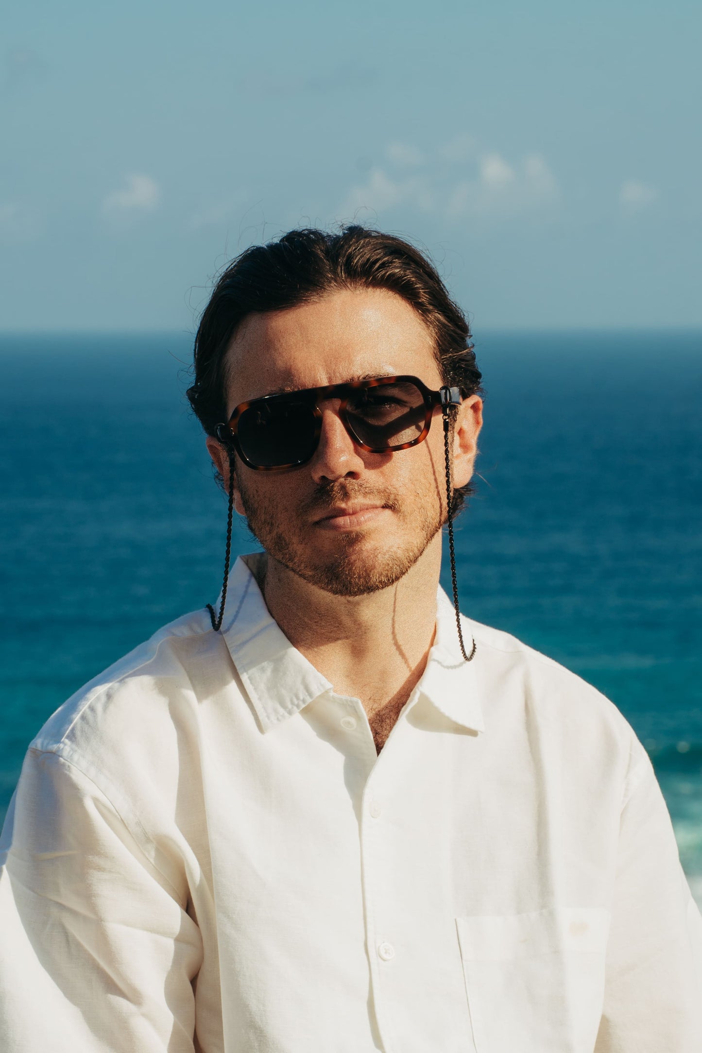 Man wearing Luxe Co. Caramel Swirl tortoise sunglasses with eyewear chain by the ocean in Bali