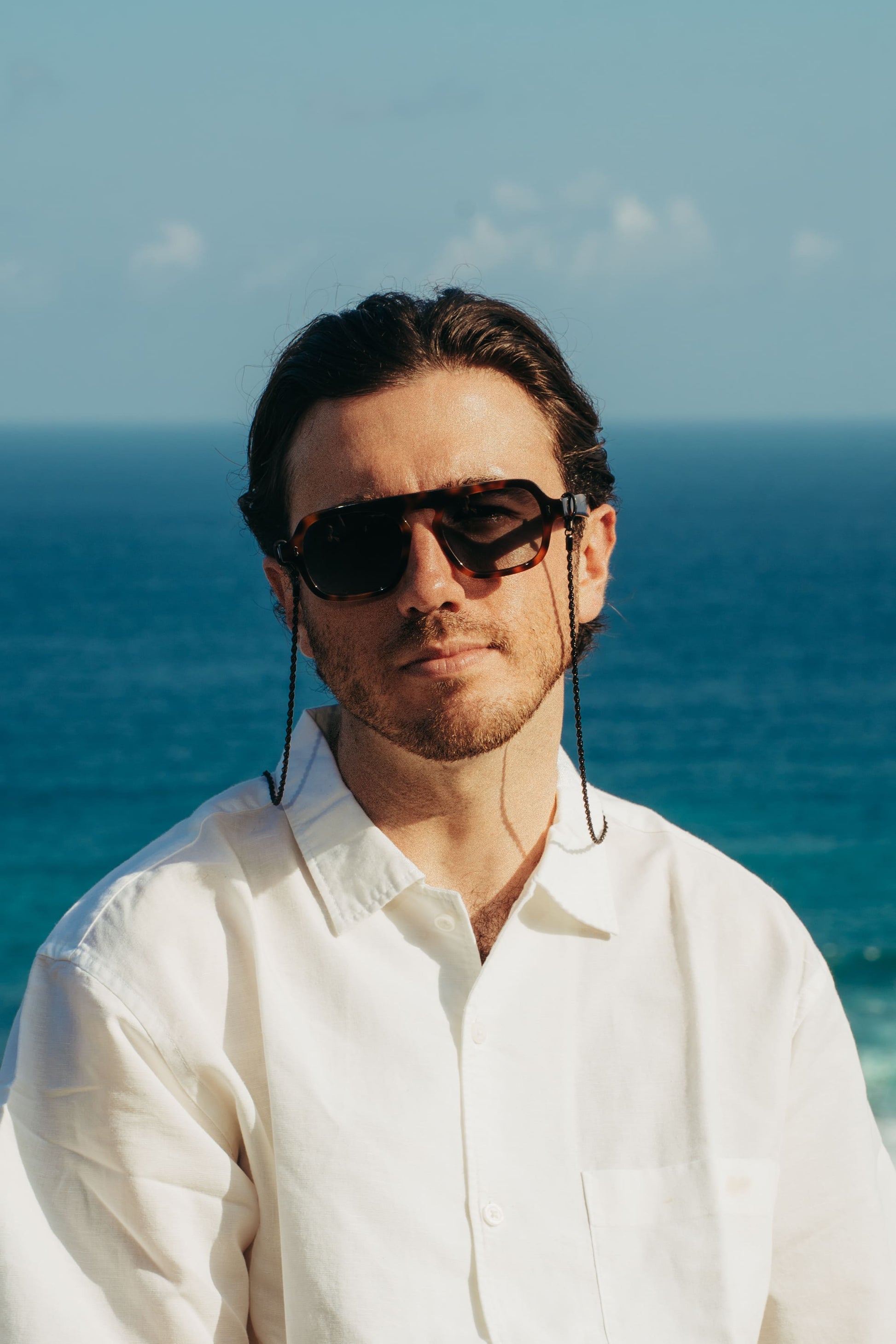 Man wearing Luxe Co. Caramel Swirl tortoise sunglasses with eyewear chain by the ocean in Bali