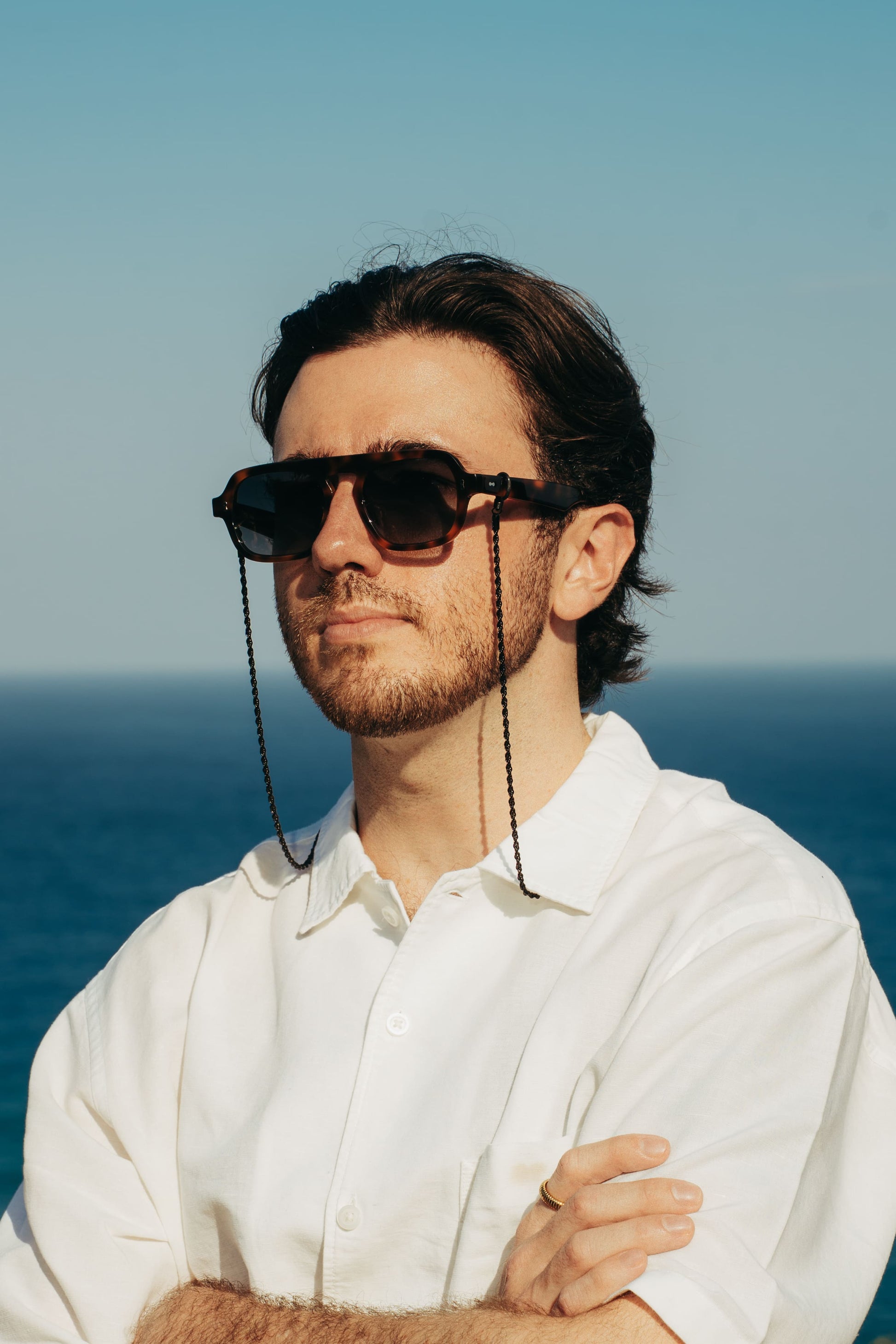 Man in Luxe Co. Caramel Swirl tortoise sunglasses and eyewear chain on the Bali coastline, Maison Mata