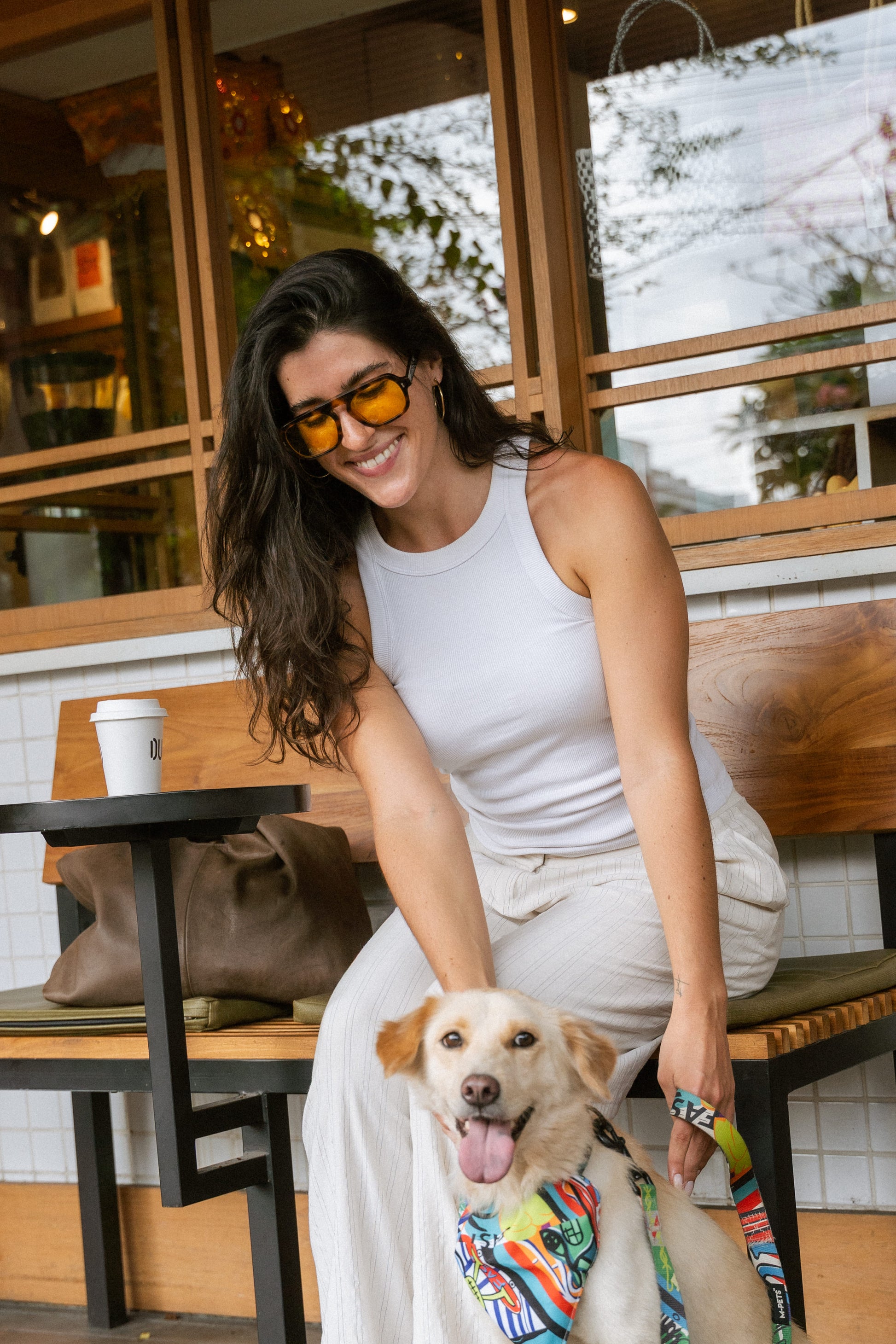Woman in Luxe Co. Caramel Swirl yellow-tinted sunglasses sitting with her dog at a Bali café